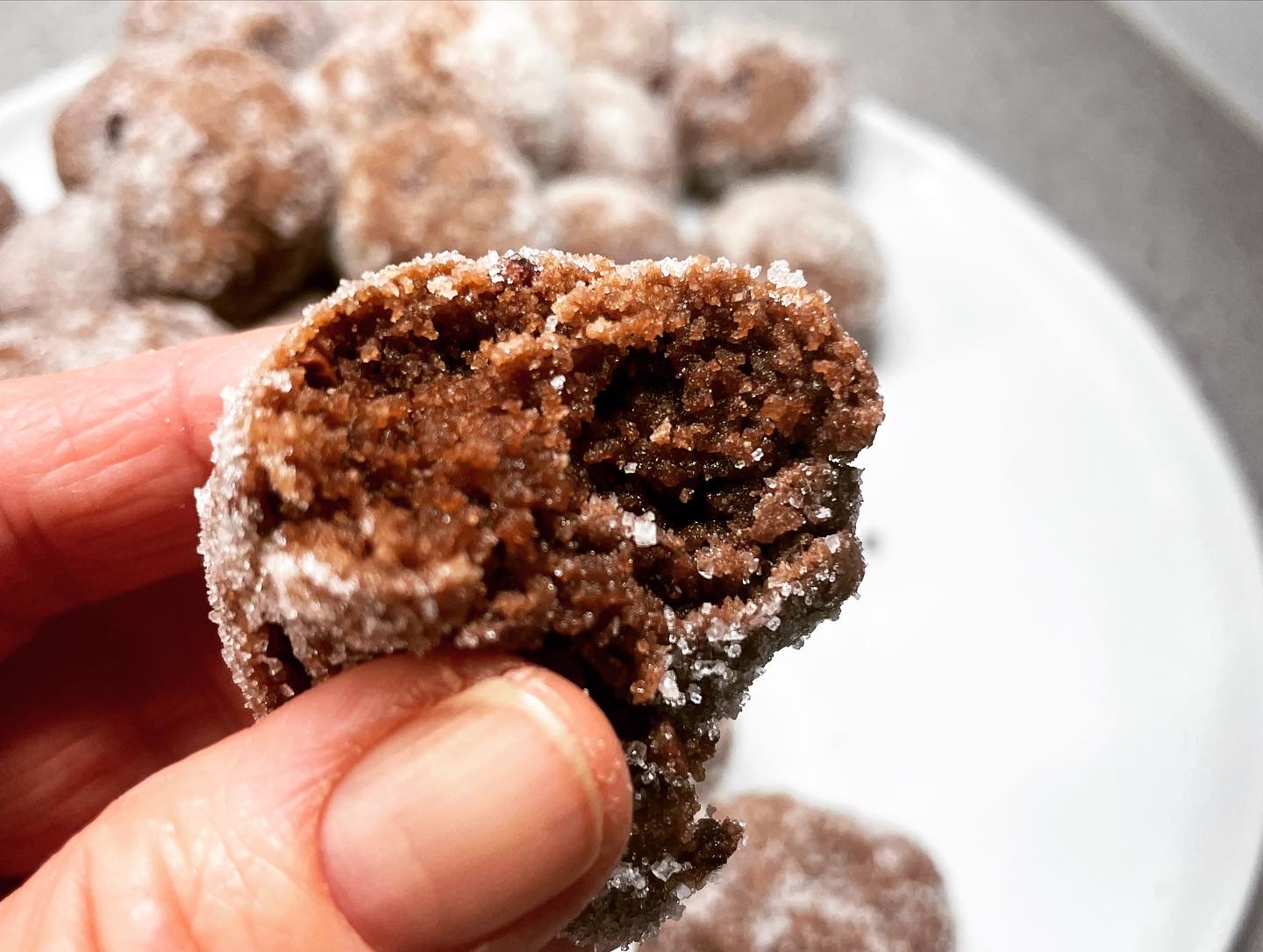 Close-up image of a caucasian hand holding a dark donut bite with a bite taken out of it.