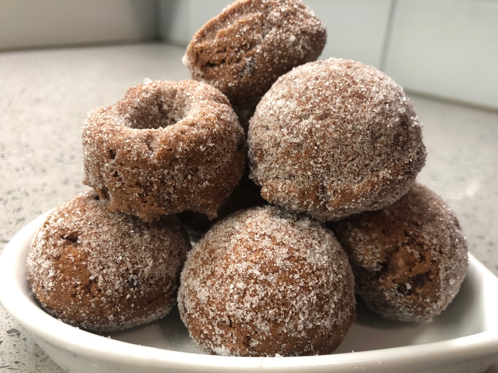 Image of dark, round donut cacao, five-spice donut piled high on a white plate.