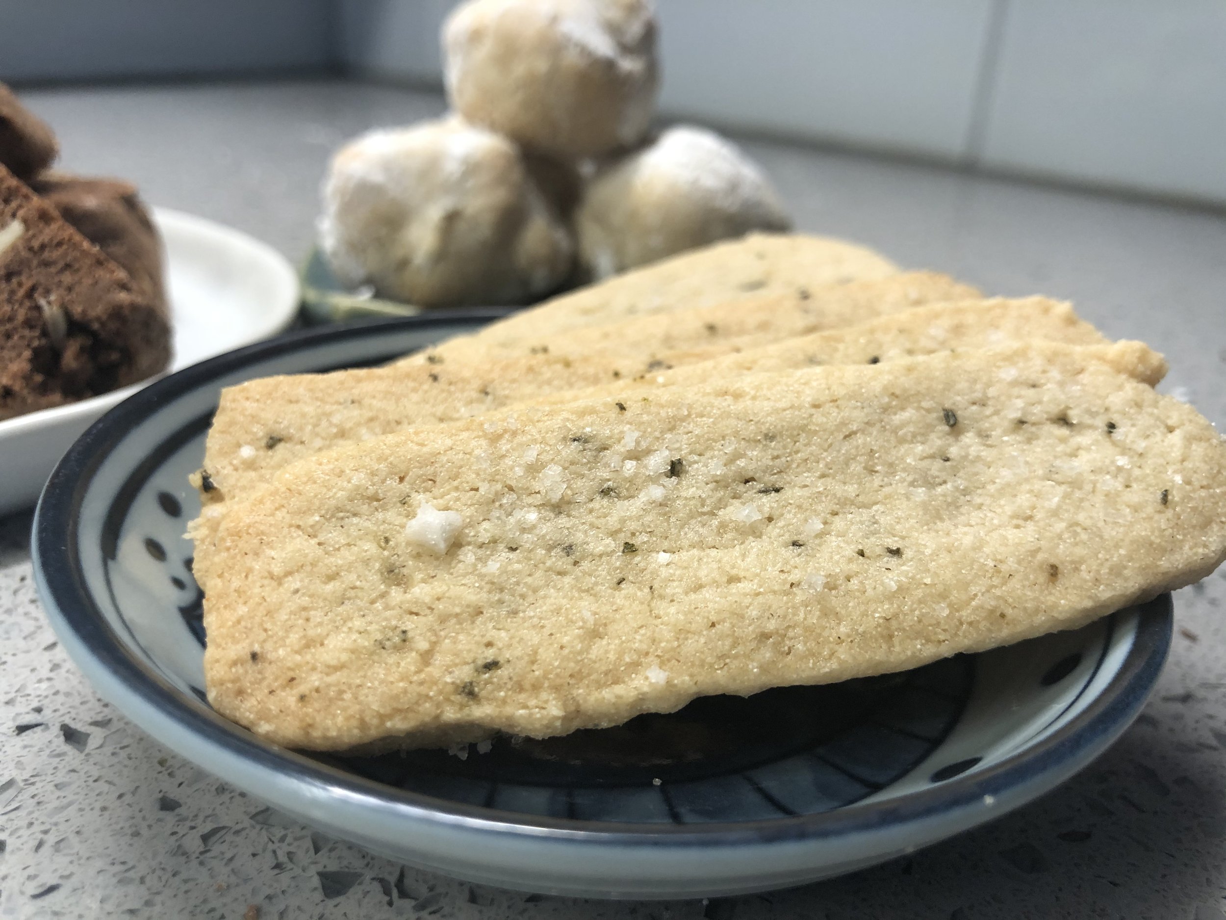 Light colored rectangular rosemary sea salt batons on a dark colored plate.