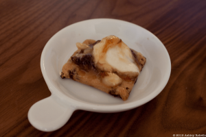 Image of savory square cookie with white cream and caramel on top in a white bowl with a flat handle.