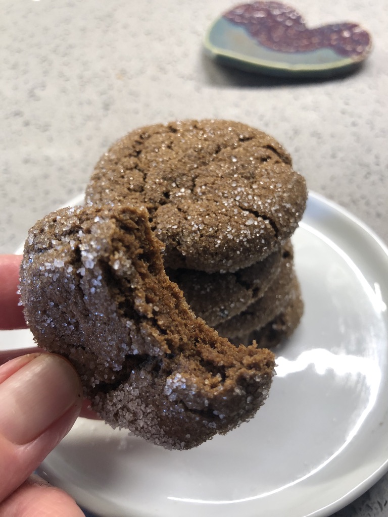 A small stack of ginger snap cookies with one half-eaten cookie being held by a hand.