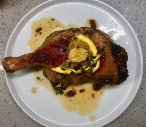 Image of a cooked duck leg with lemon, garlick and sauce.