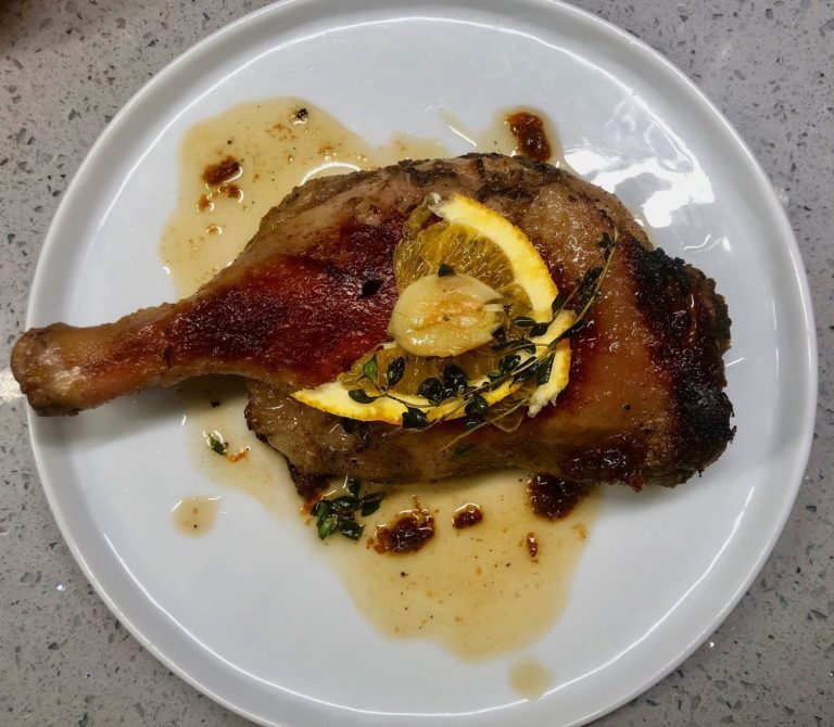 Image of a cooked duck leg with lemon, garlick and sauce.